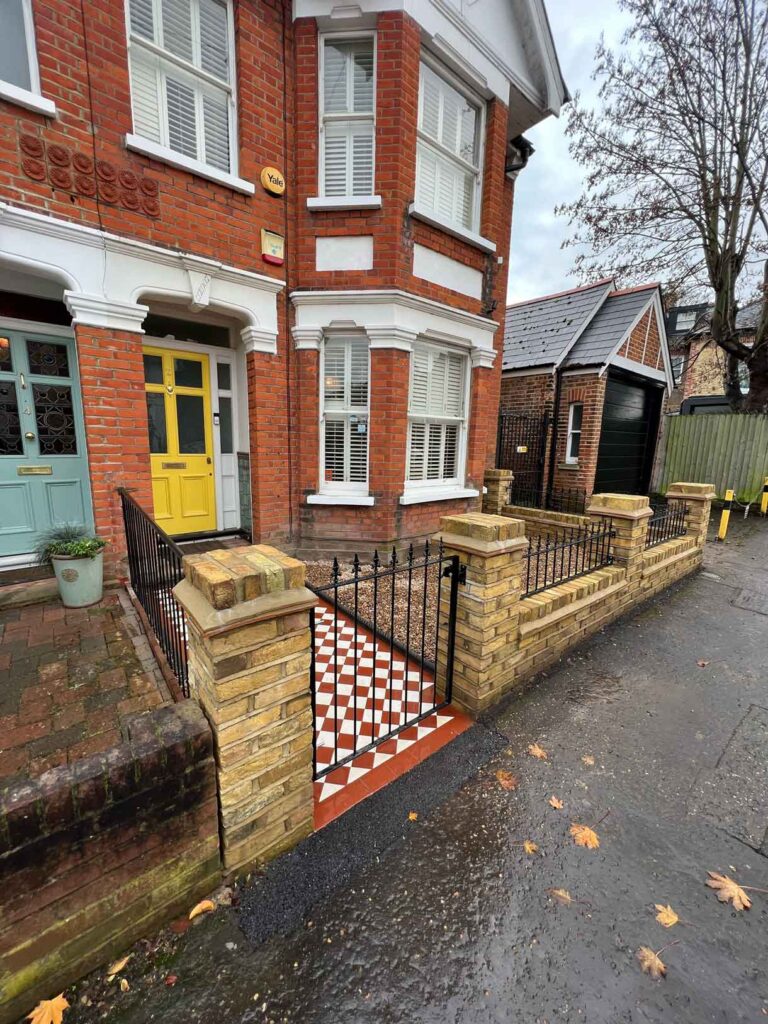A yellow brick wall and a red and white victorian path in checkerboard style.