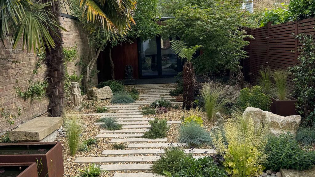 A gravel garden with plants and boulders, a water feature and stepping stones.