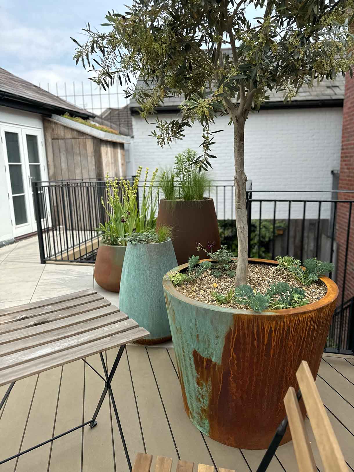 Seating area on roof terrace with planters and black railings.