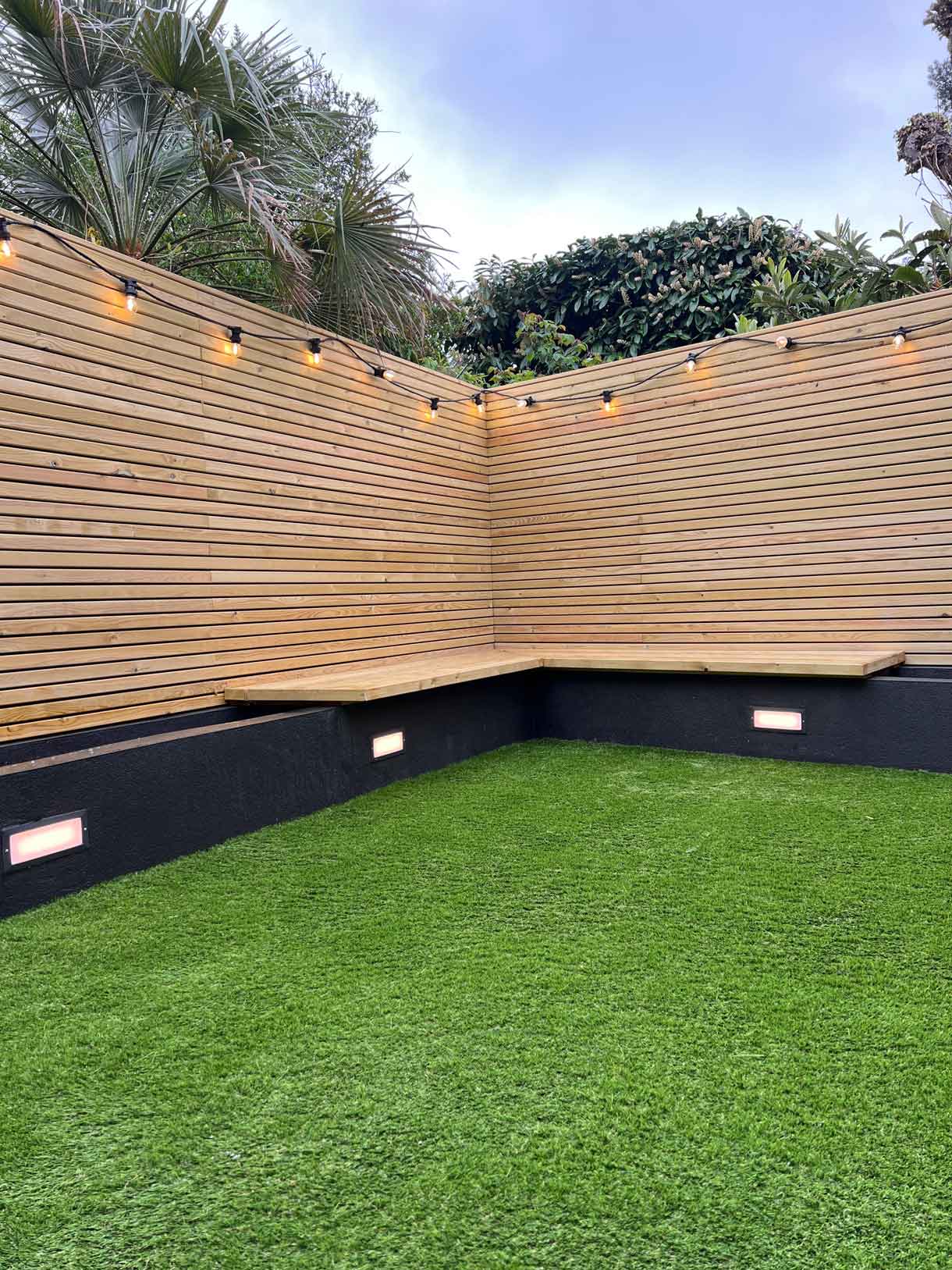 Compact lawn area enclosed by timber cladding with corner planting.
