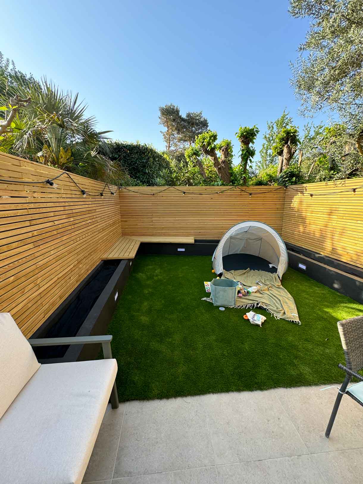Courtyard garden with children’s play tent and lawn surrounded by timber battens.