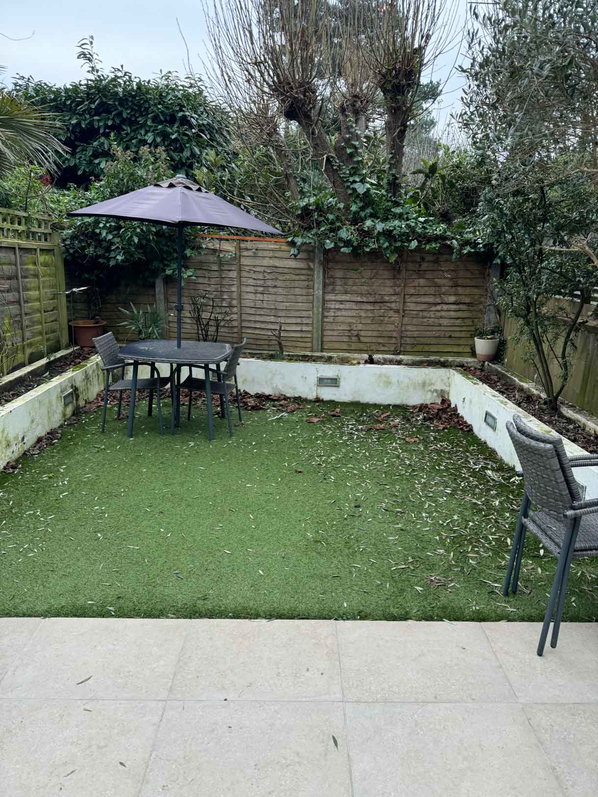 Small dining table with umbrella in courtyard garden before renovation.