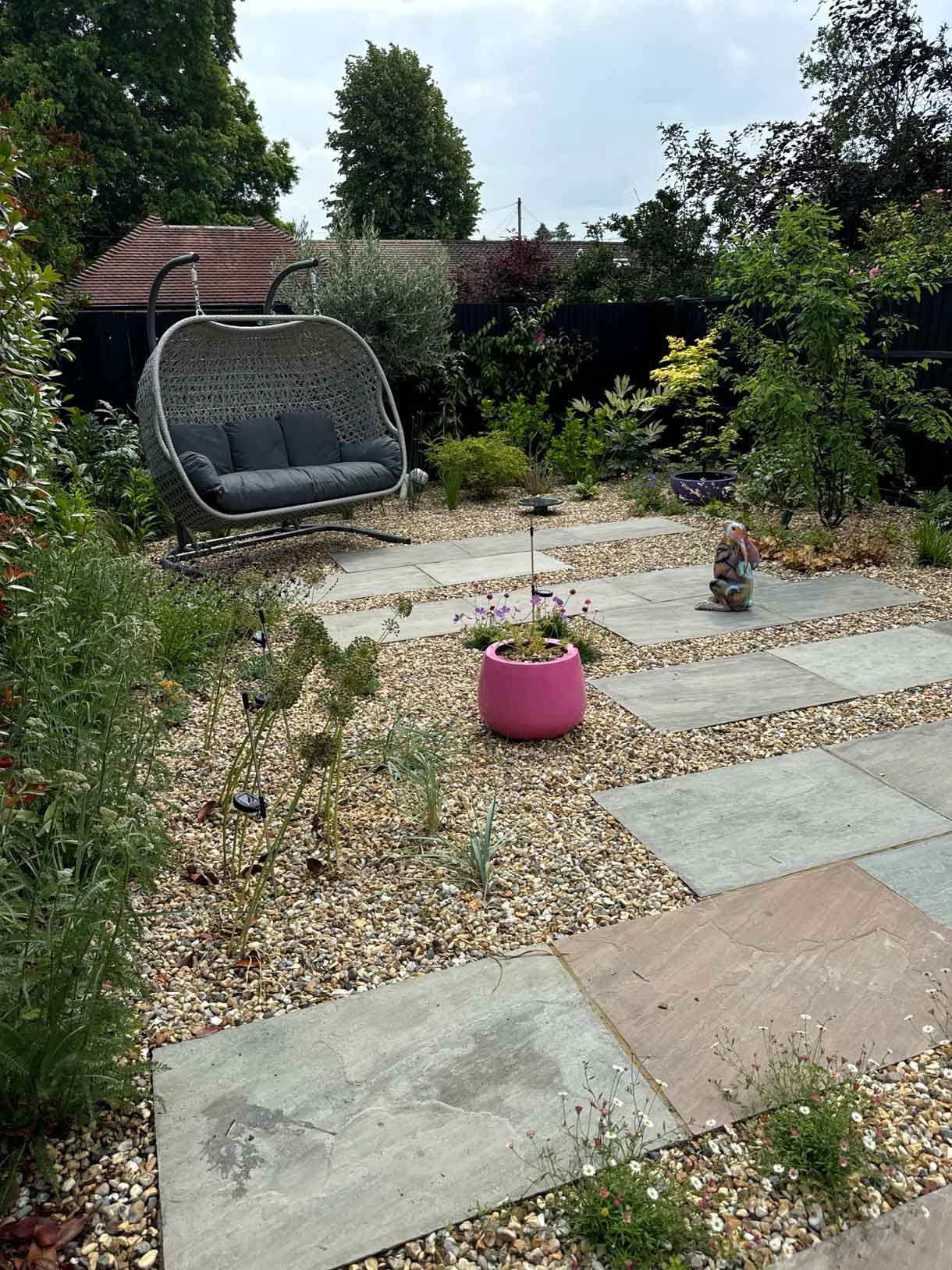 Swing seat and pink planter in gravel garden with staggered paving.