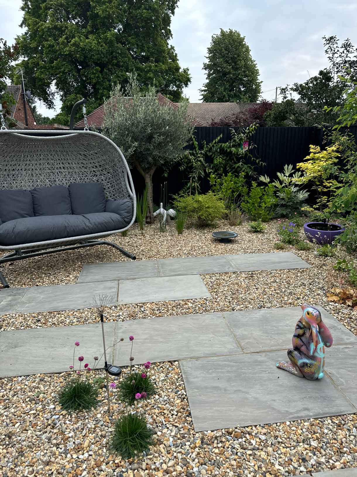 Swing seat and colourful rabbit ornament in gravel garden with staggered paving.