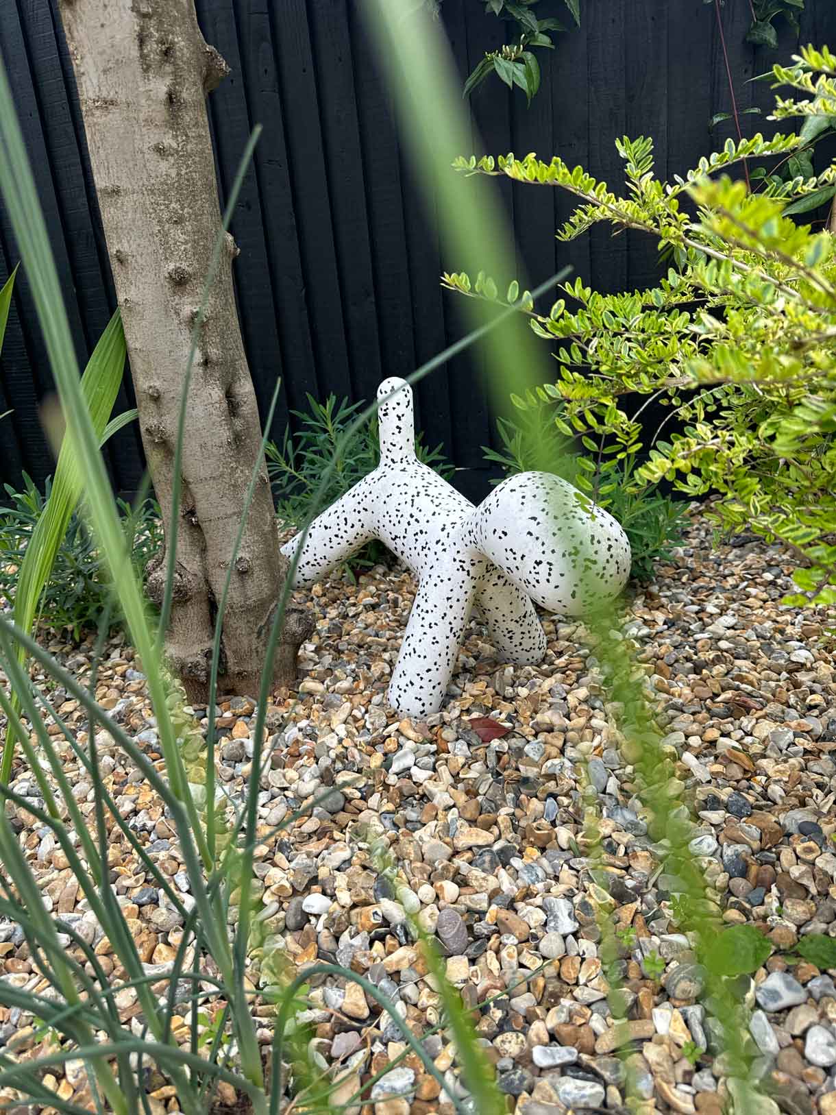 White decorative dog sculpture placed among gravel and planting.