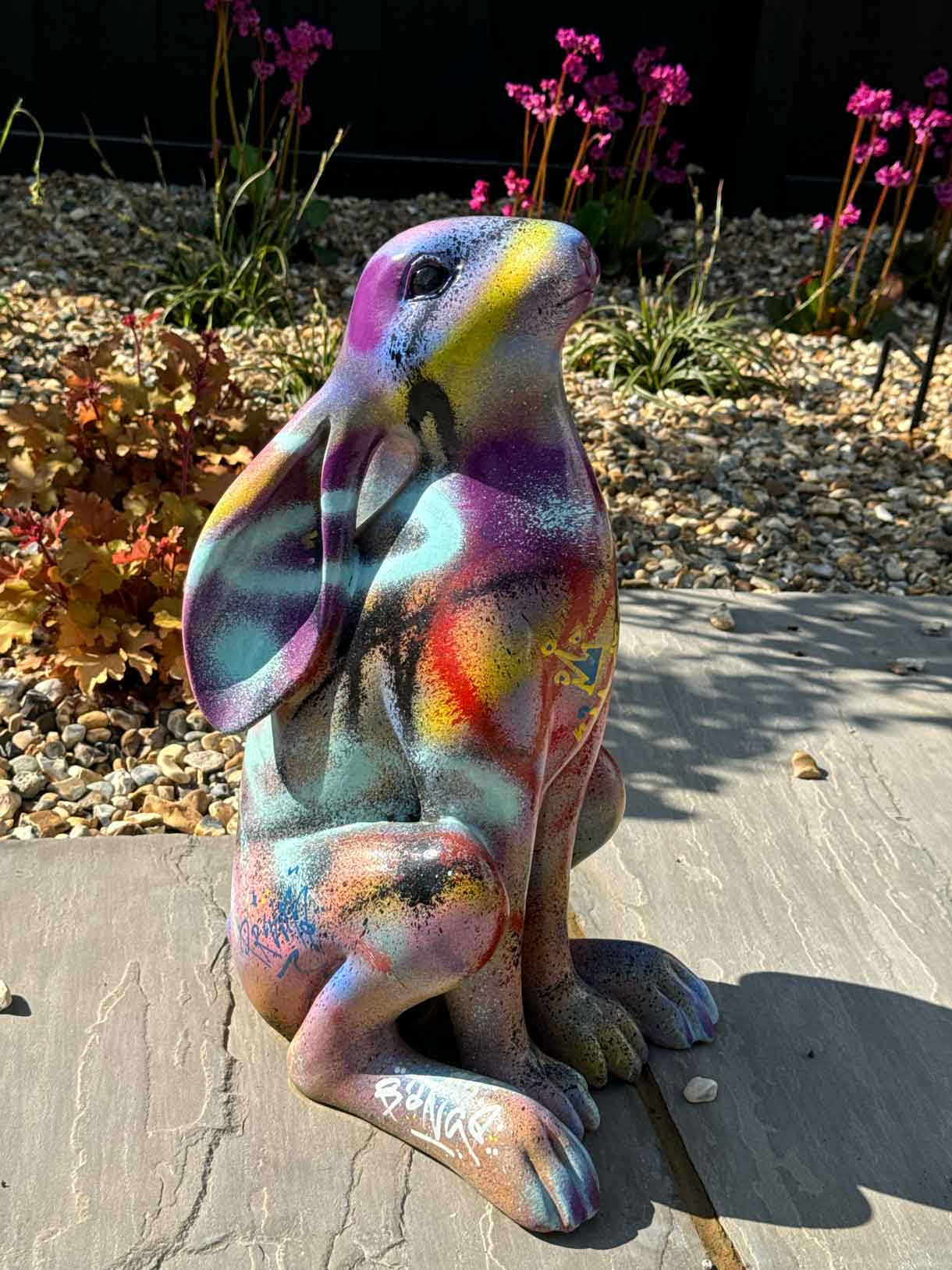 Colourful painted rabbit ornament placed on a garden paving stone.