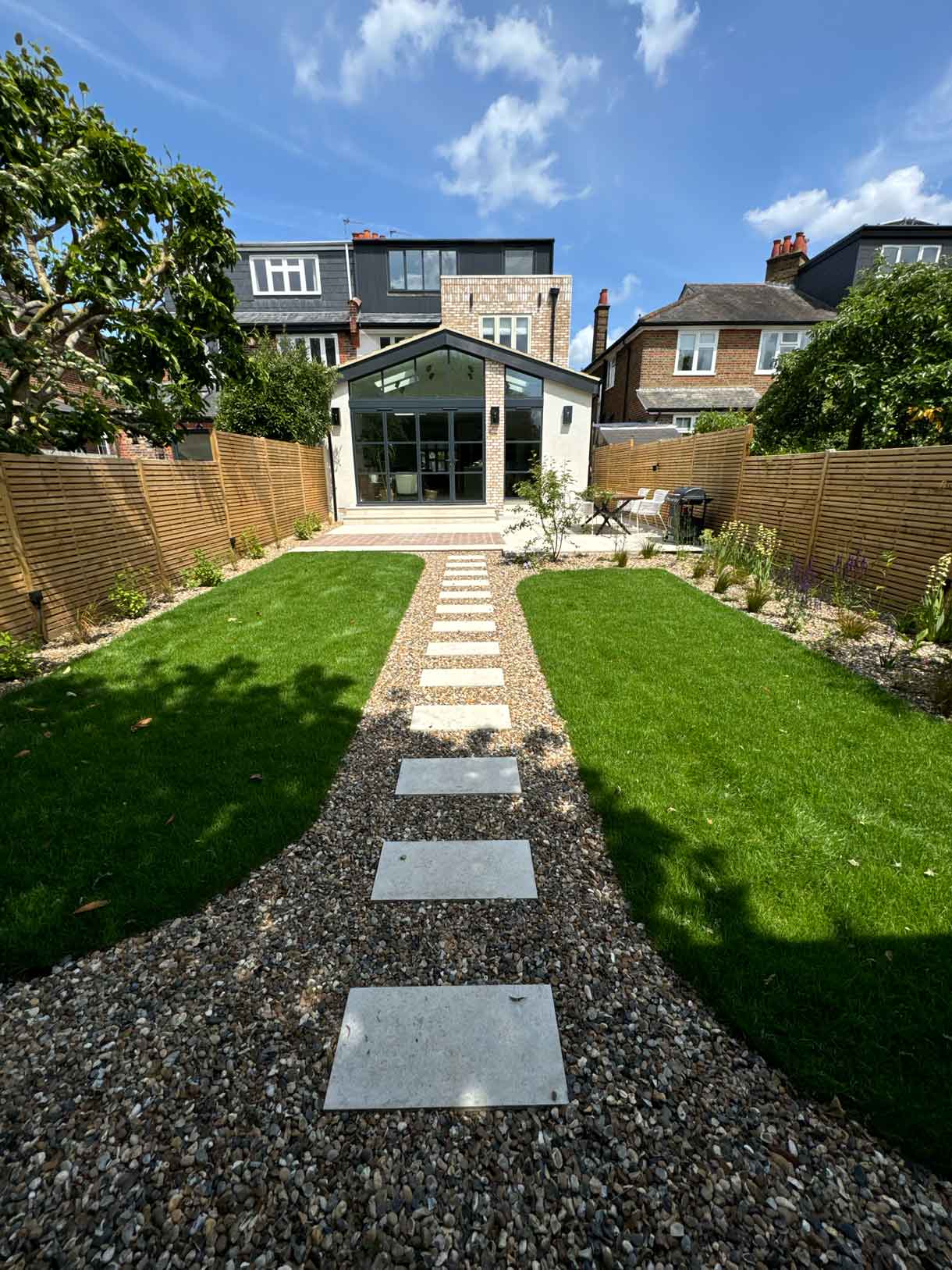 Garden path leading across lawn toward modern house extension.