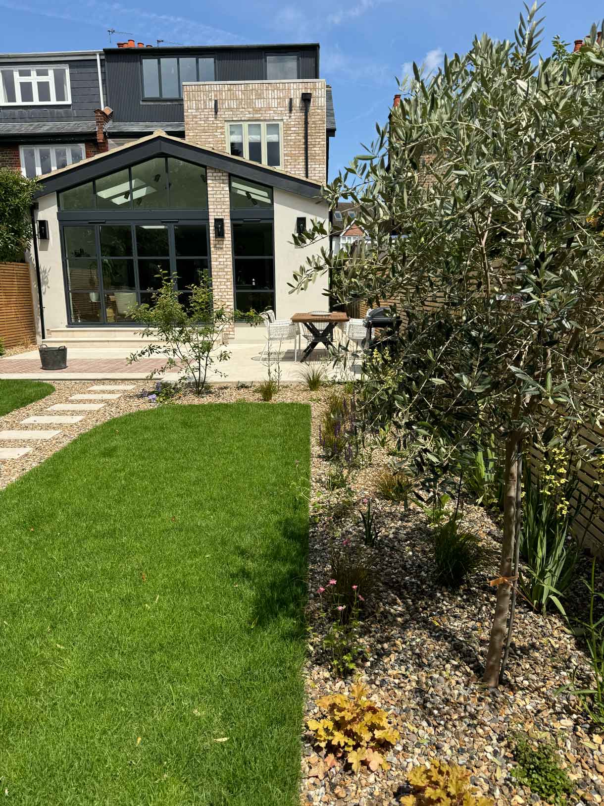 Garden path leading to modern garden room framed by olive trees.