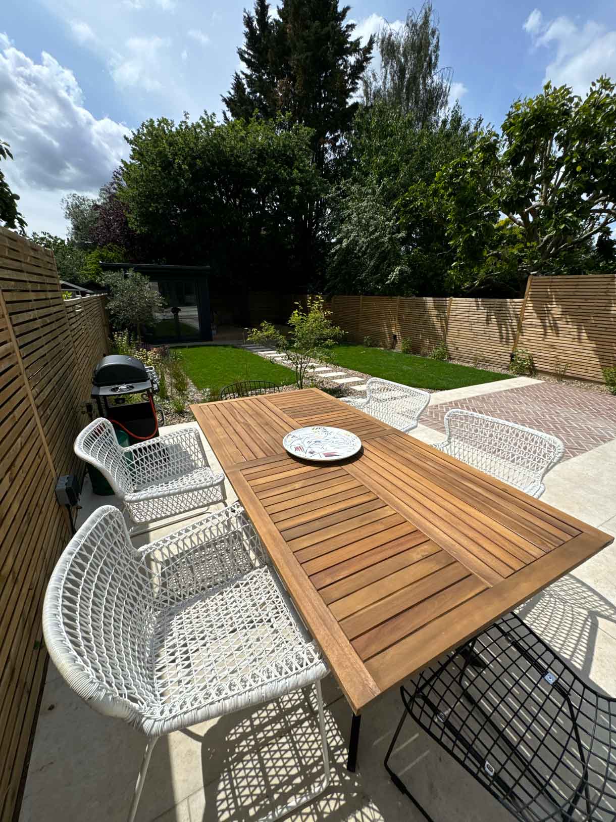 Outdoor dining table with barbecue beside lawn and garden path.