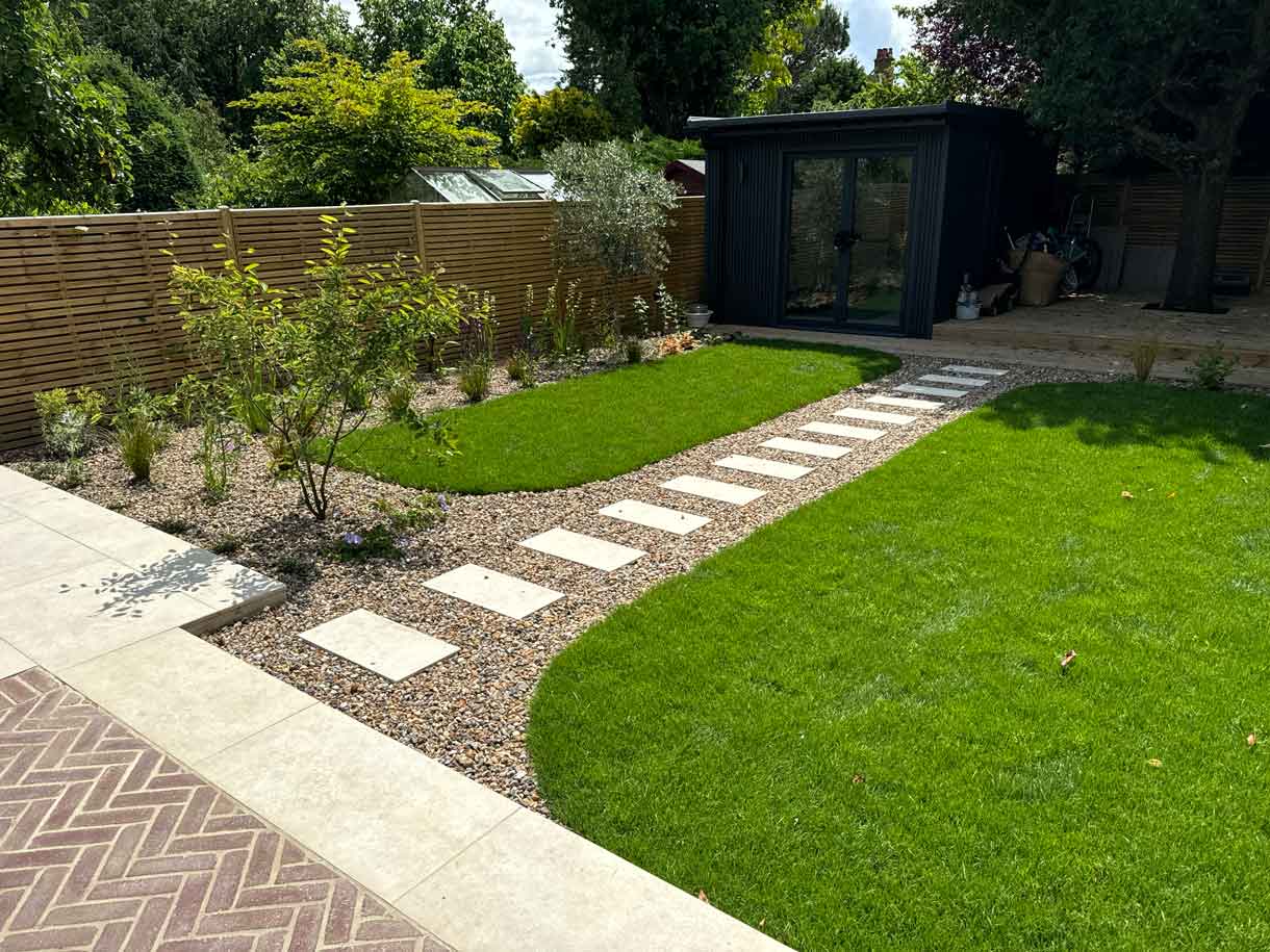 Stepping stone path cutting through lawn toward black garden studio.