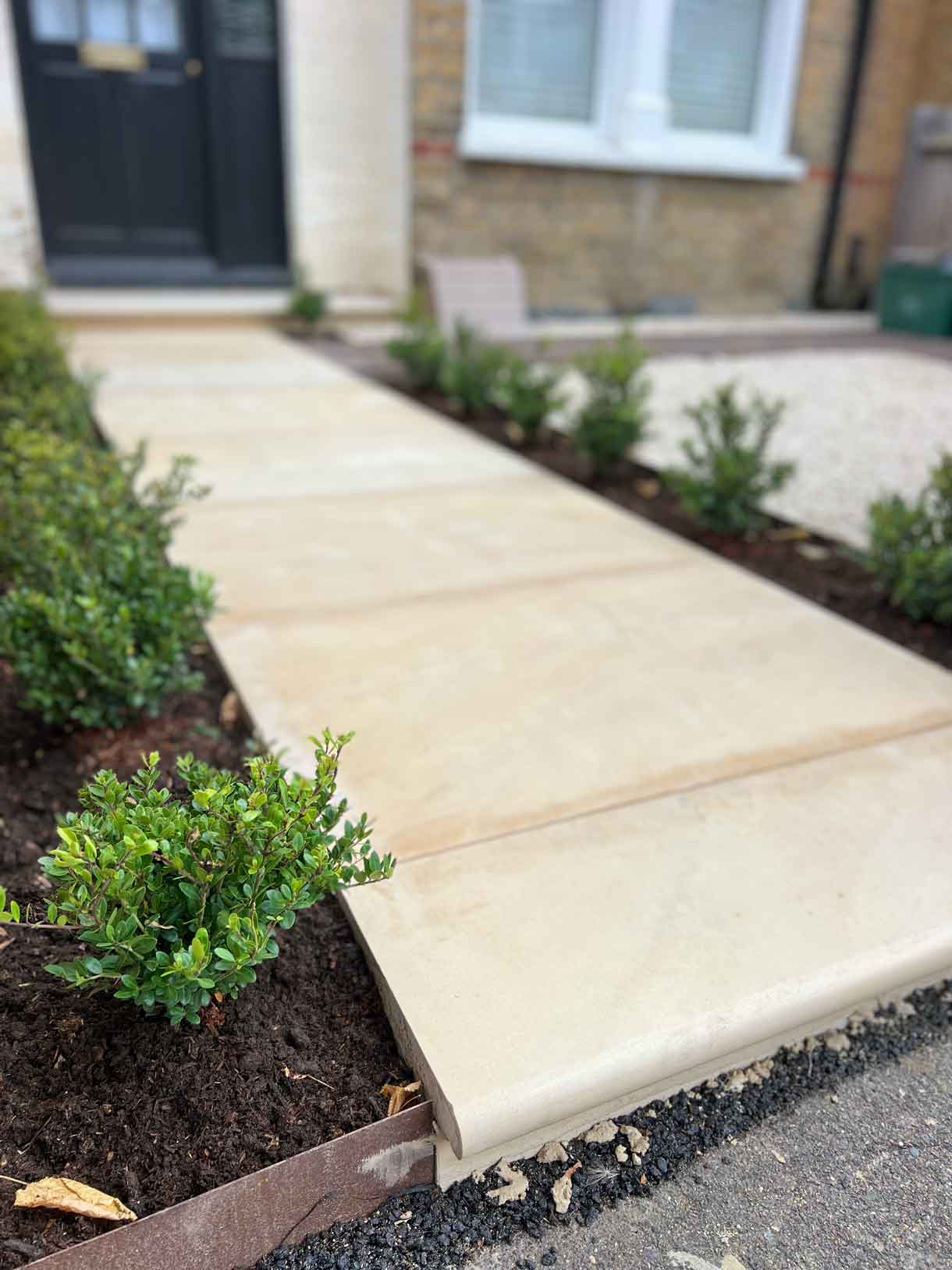 Finished sandstone path leading directly to the black front door.