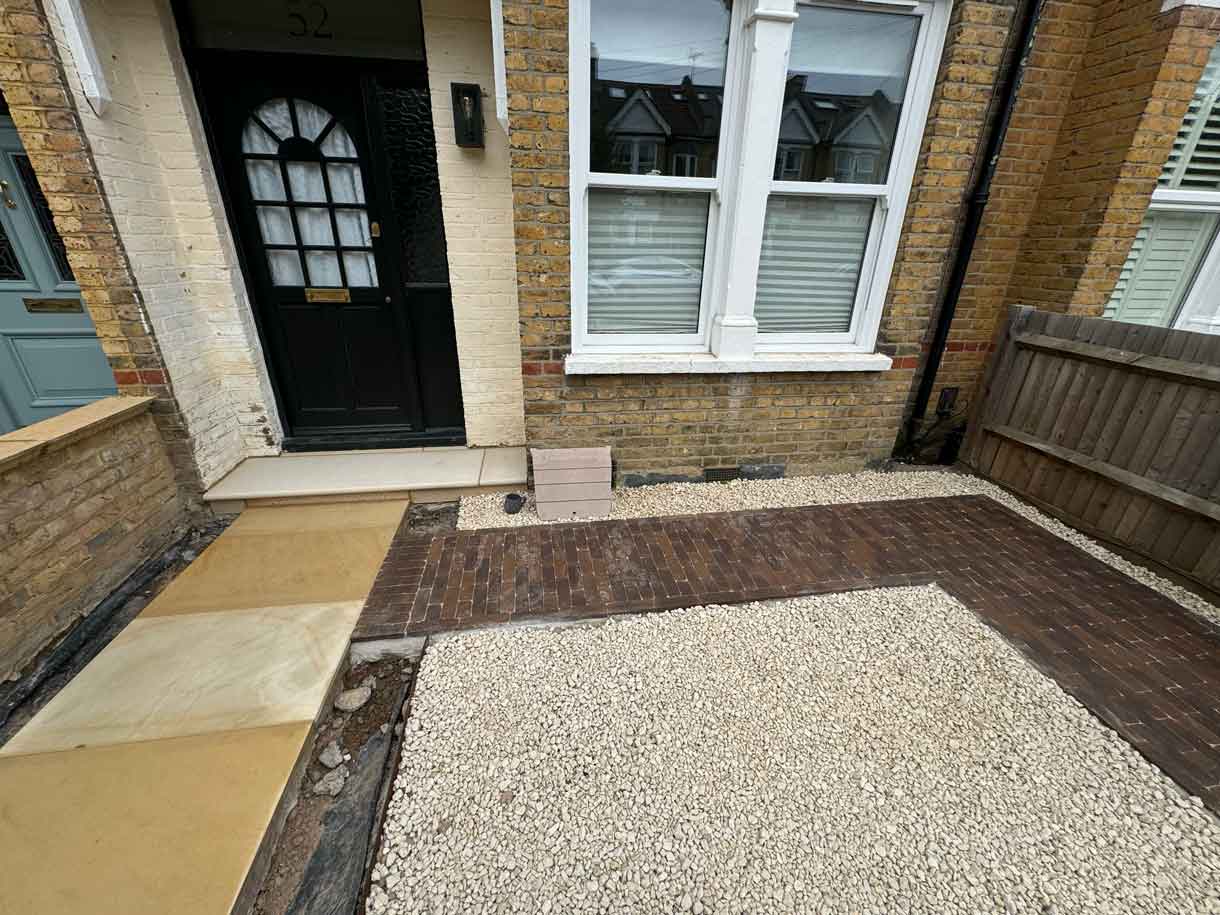 Front path with sandstone paving leading to a black front door and brick façade.