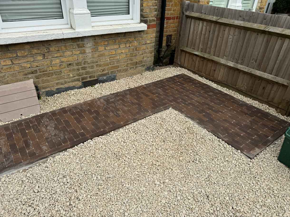 Front garden corner with gravel, brick edging and timber fence panel.