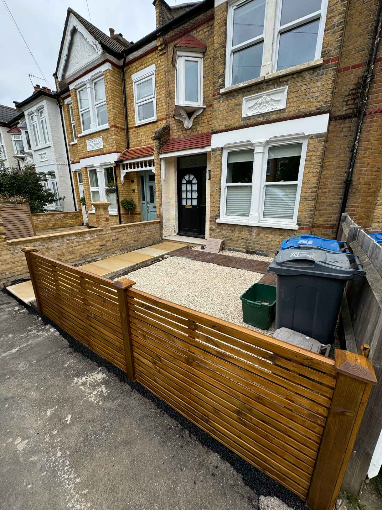 Front garden with raised timber bin store and gravel surface.