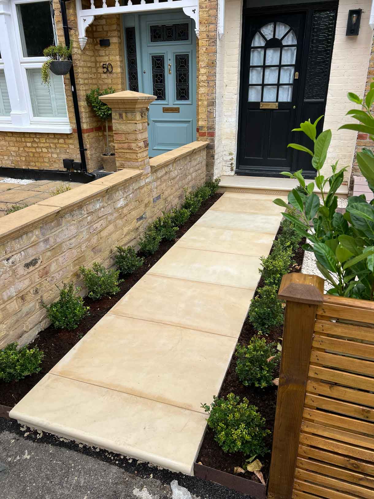 New sandstone path bordered by raised brick planters in the front garden.