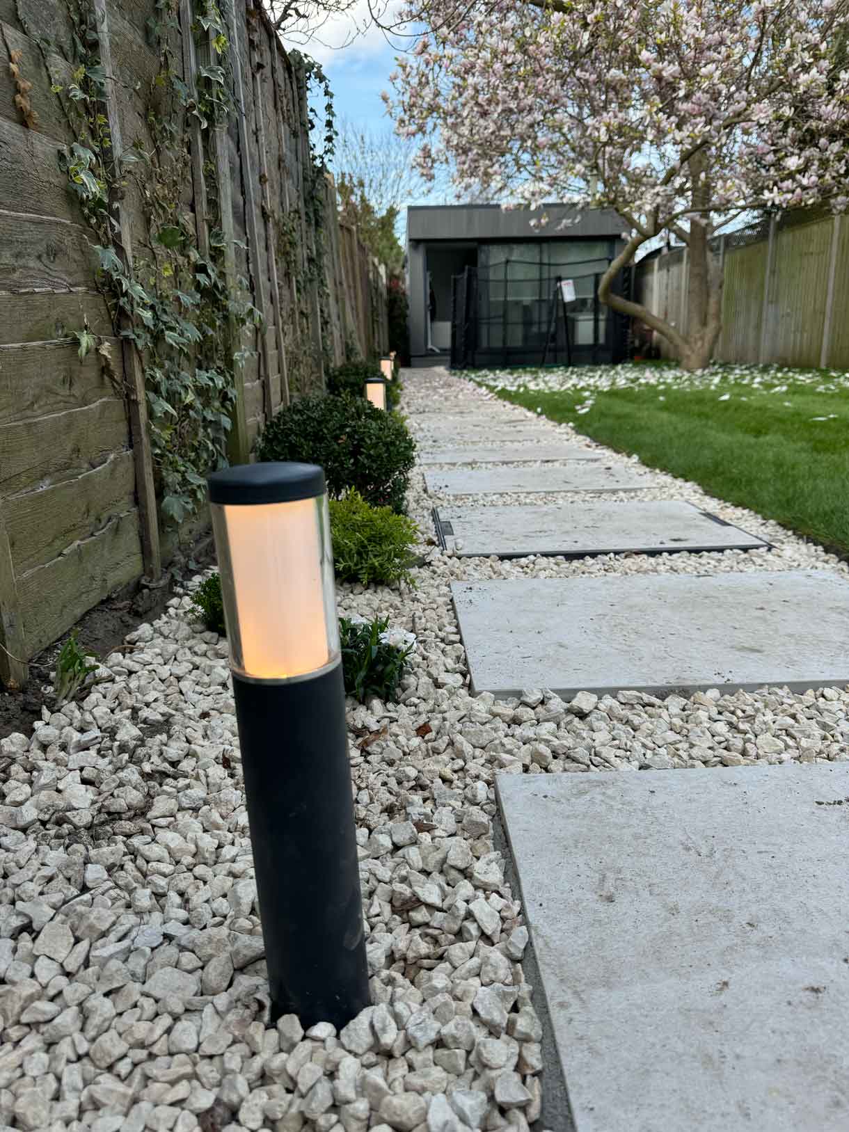 Stone path leading down a long garden with magnolia tree and trimmed borders.