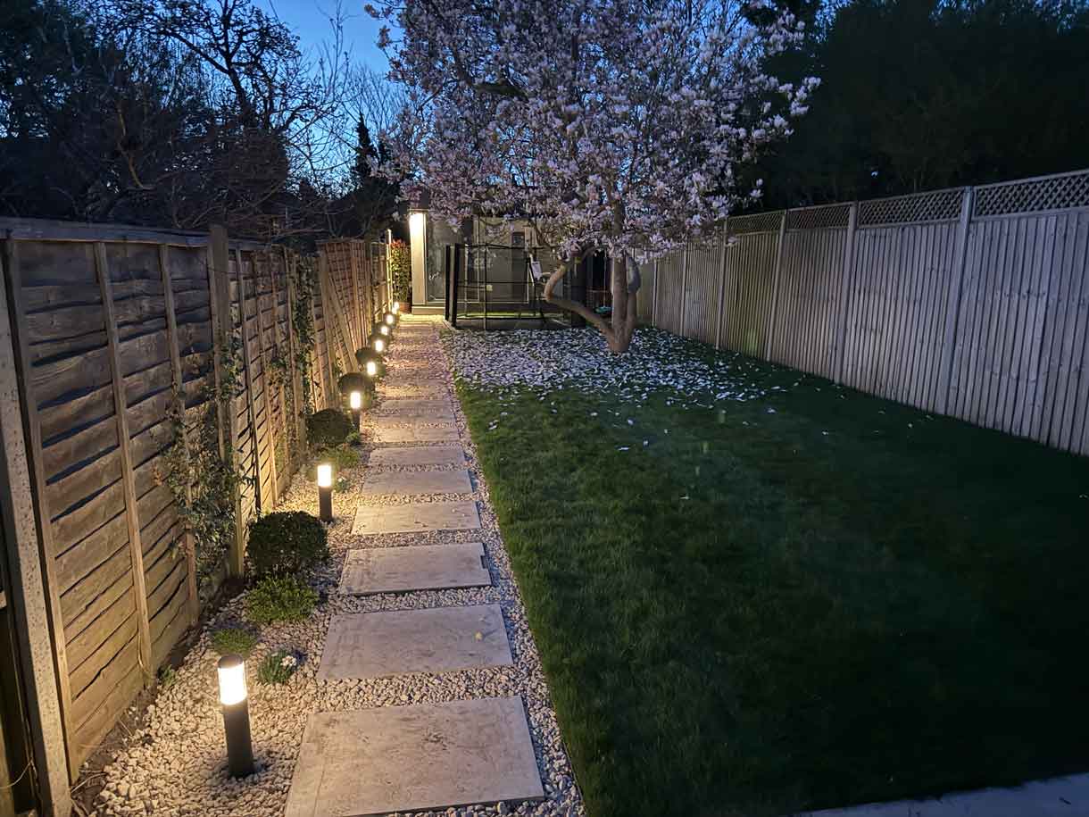 Gravel and stepping-stone path lined with low bollard lights along a timber fence.