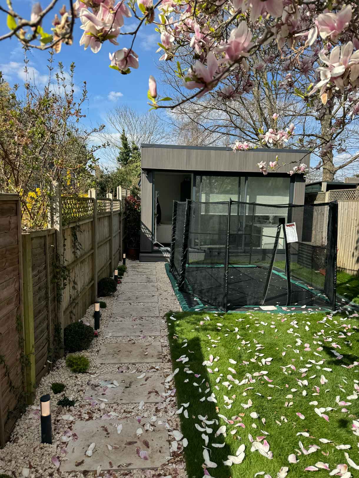Garden entrance view with magnolia petals scattered across the lawn and path.