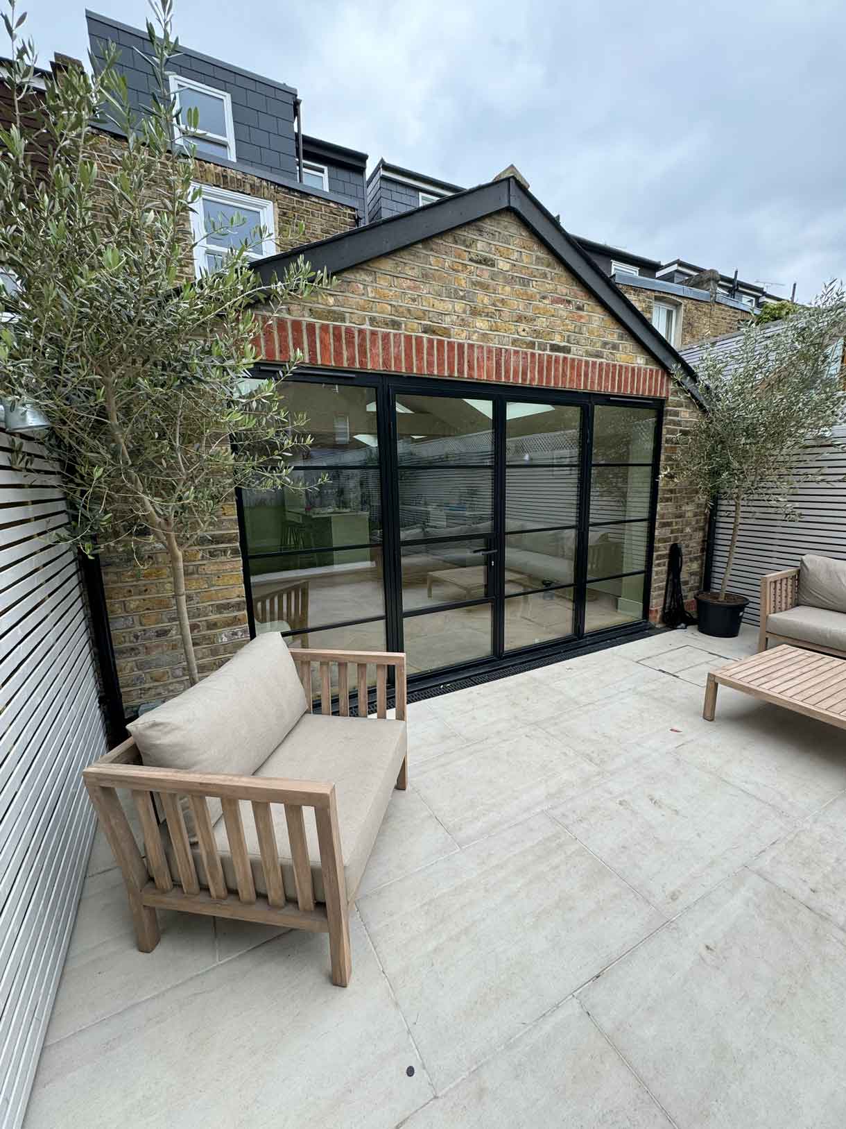 Garden room with black-framed glazing opening onto a paved patio with seating.