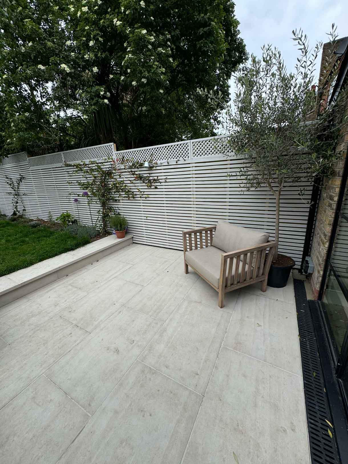 Wide paved patio with seating area beside white slatted garden fence.