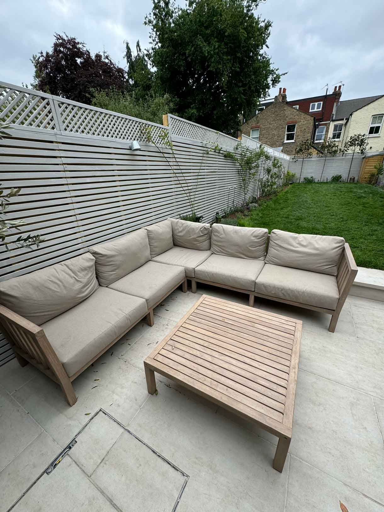 Lawn and raised patio with garden seating against white slatted fencing.