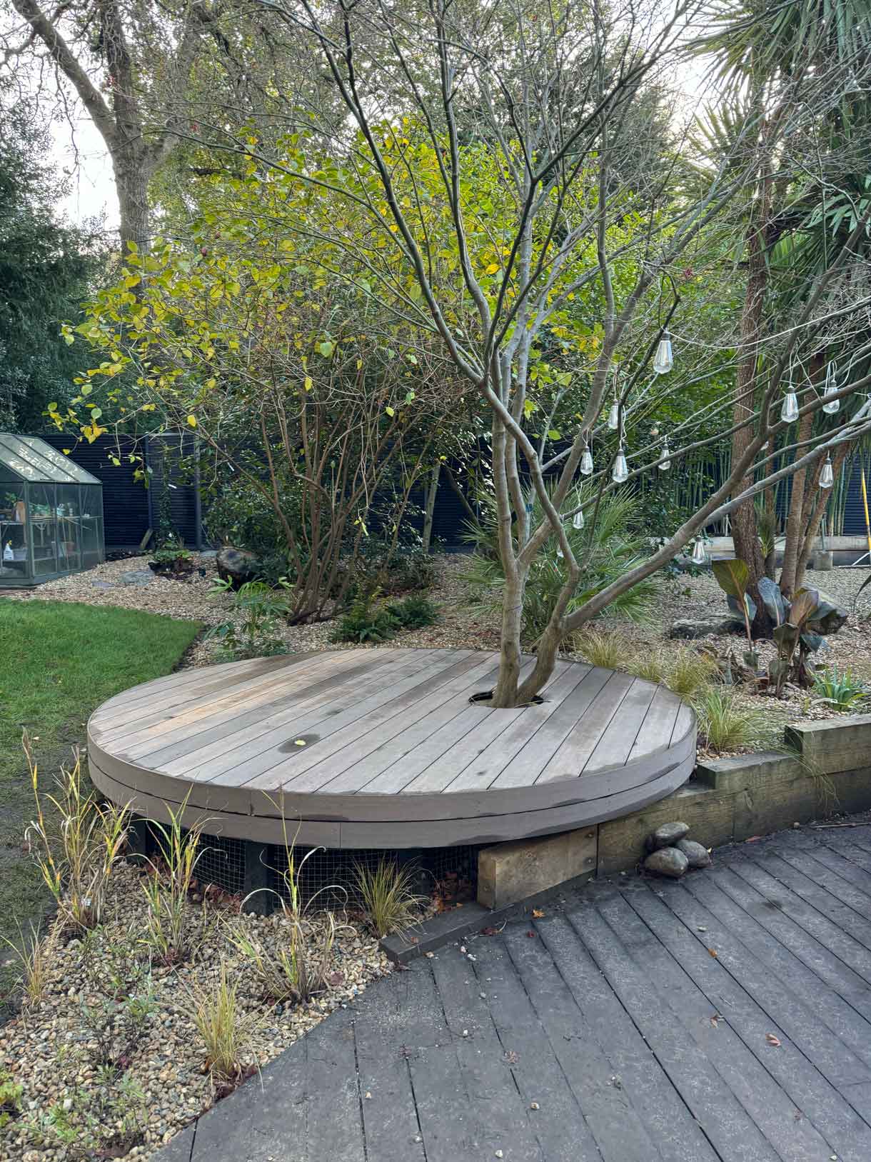 Circular timber seating platform set within a woodland-style garden.