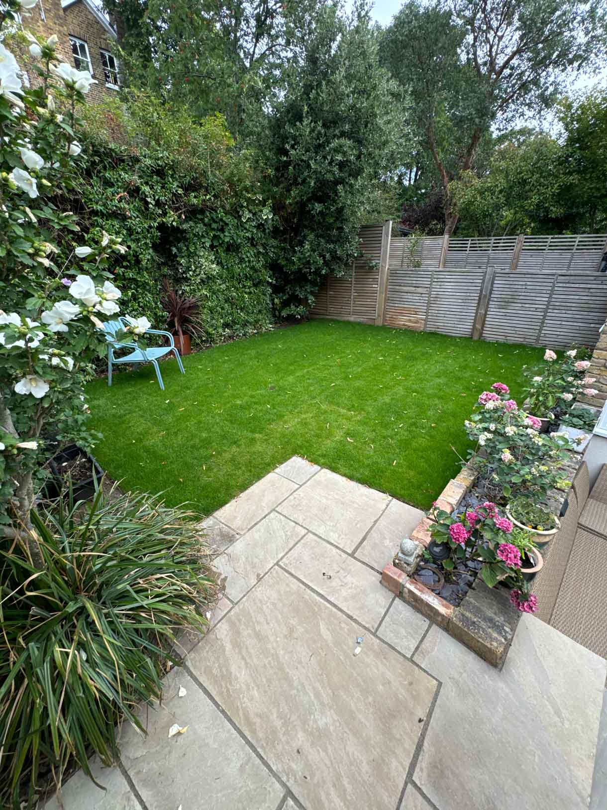 Rear garden with paving, lawn and a shaded corner planting bed.
